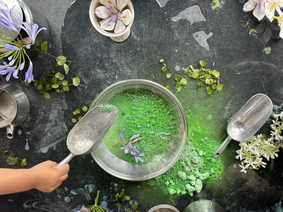 Child exploring a green sensory activity with flowers, water and natural materials